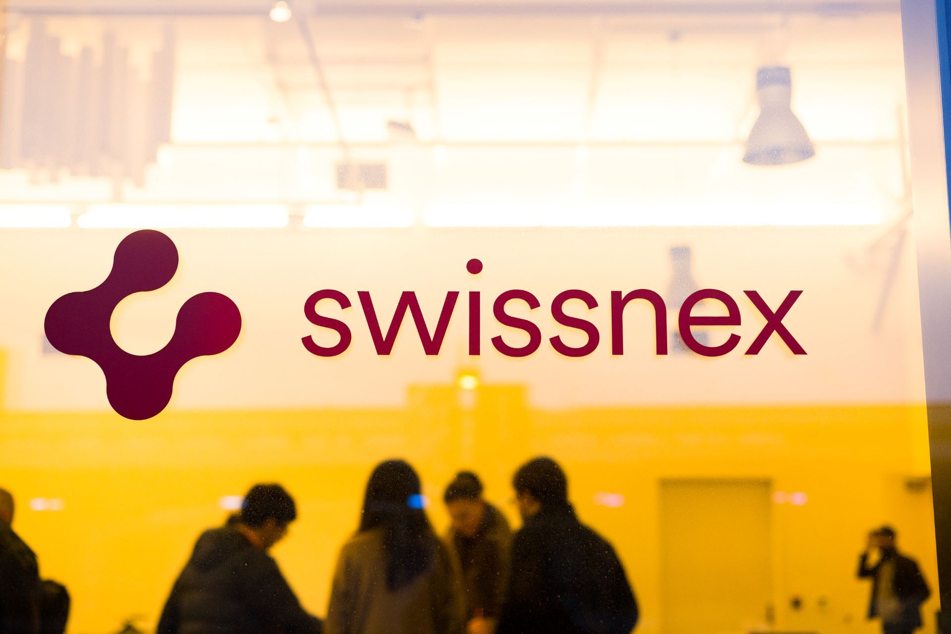 Стеклянная дверь офиса Swissnex и люди, занятые обсуждением, на заднем плане