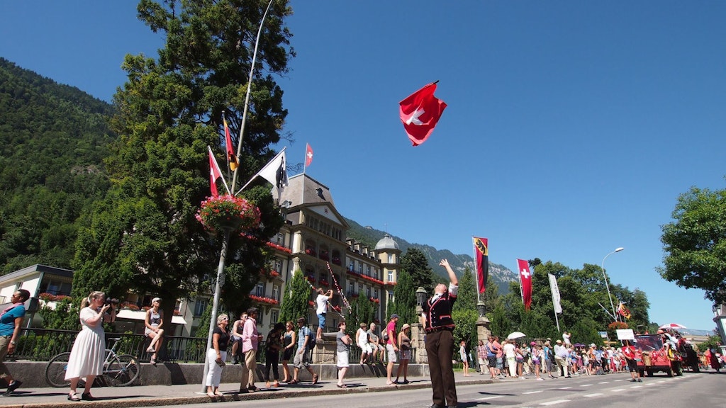 Homme en costume traditionnel brandissant un drapeau suisse.