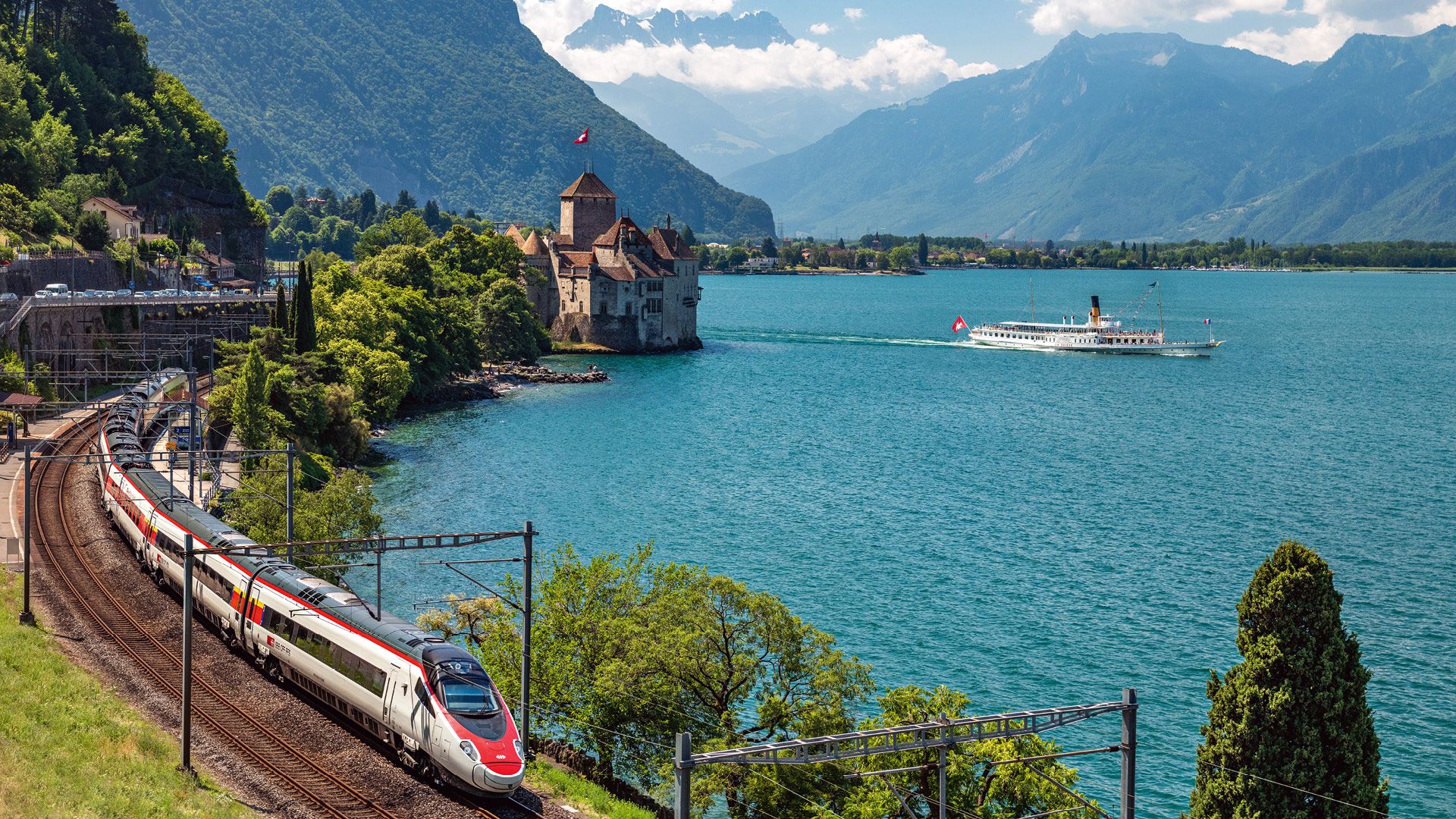 A modern Intercity train of Switzerland's federal railways company. On Lake Geneva, a scheduled boat is on its way from Chillon Castle towards Montreux.