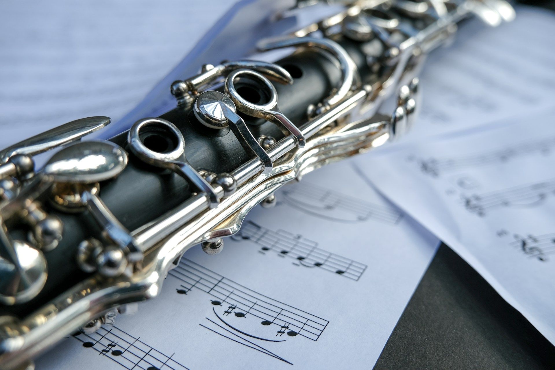 Close-up of a clarinet’s body and silver keys resting atop scattered sheet music.