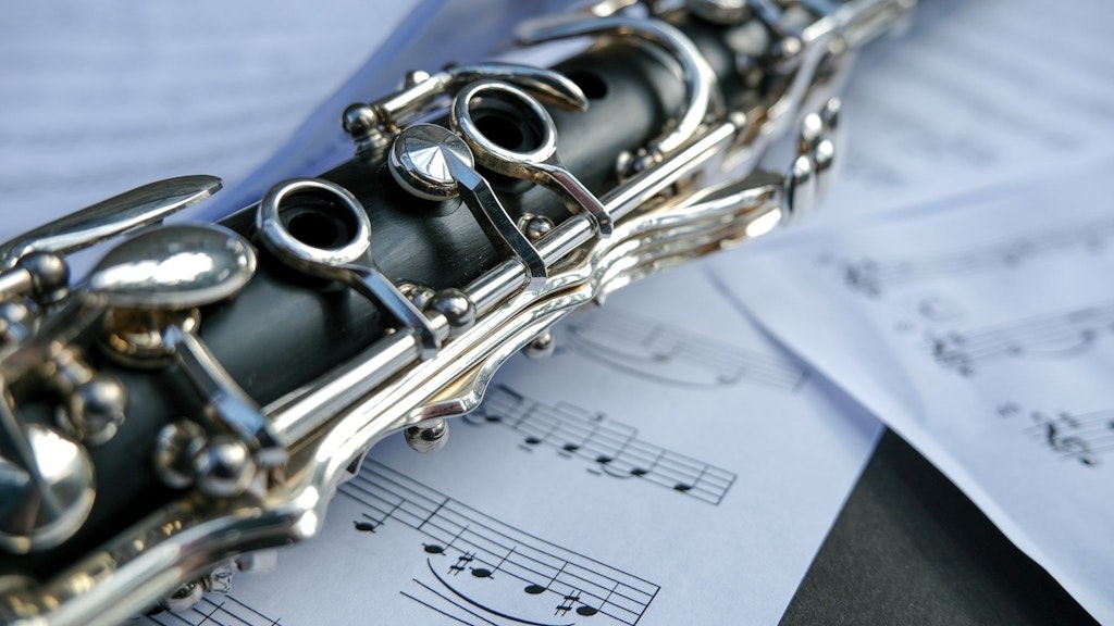 Close-up of a clarinet’s body and silver keys resting atop scattered sheet music.