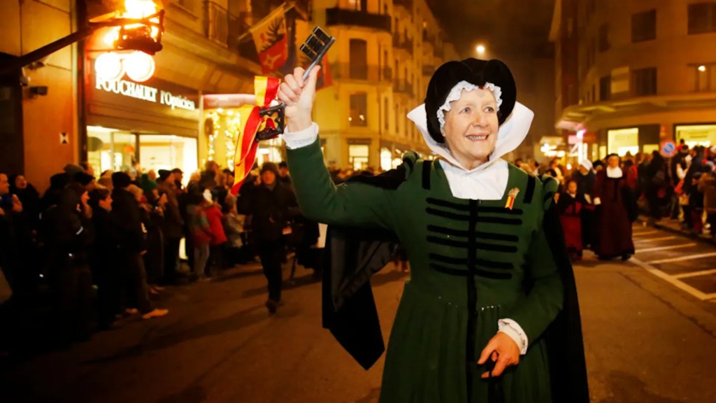Frau in grünem historischem Kostüm hält einen grossen Schlüssel bei einem nächtlichen Umzug in einer Strasse mit Zuschauern im Hintergrund.