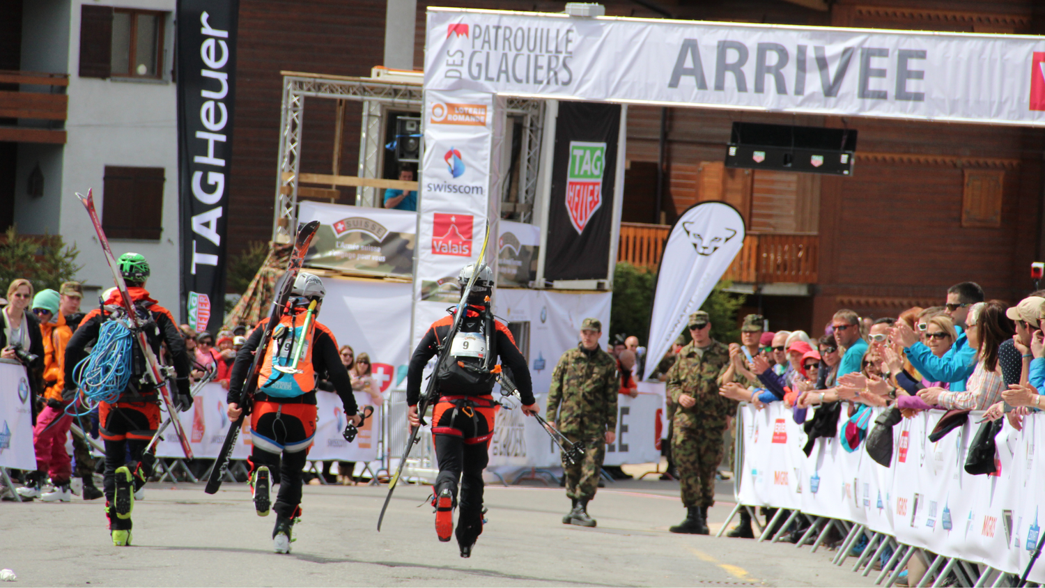 Ein Patrouillenteam überquert die Ziellinie der Patrouille des Glaciers, bejubelt von einer begeisterten Menschenmenge bei Tageslicht.