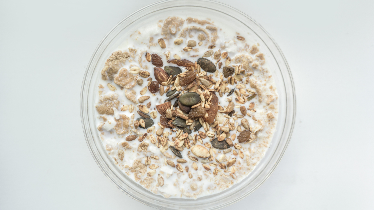 Eine Schüssel Birchermüesli mit Haferflocken, Samen, Nüssen und Apfelstücken in Milch, von oben auf einem hellen Hintergrund gesehen.