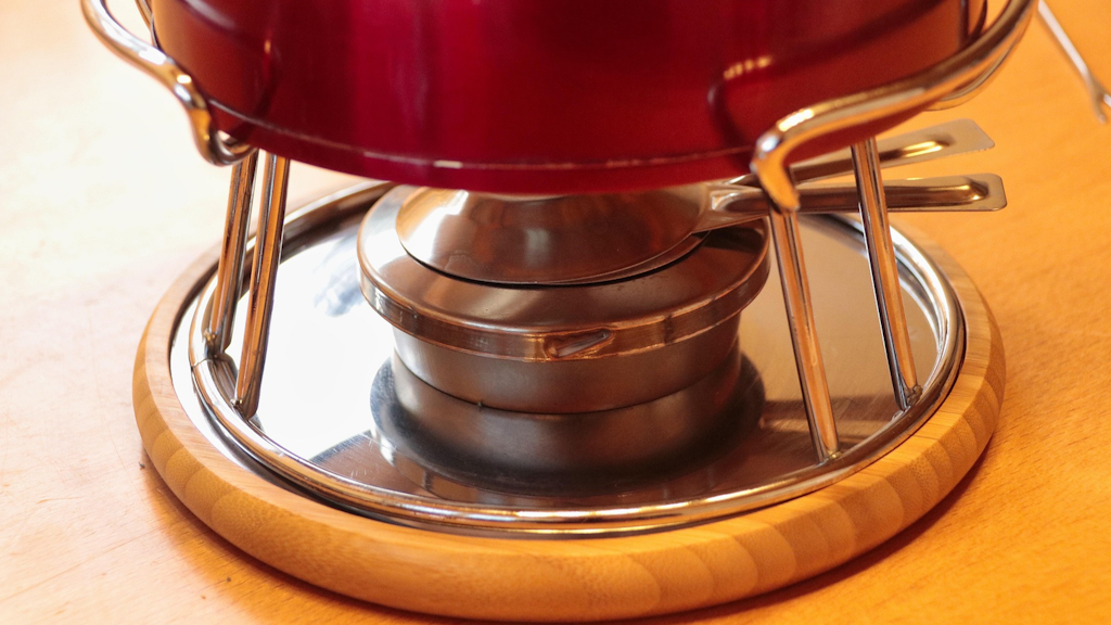 Fondue-Rechaud aus Metall und Holz mit rotem Topf darauf, in Nahaufnahme auf einem Tisch. 