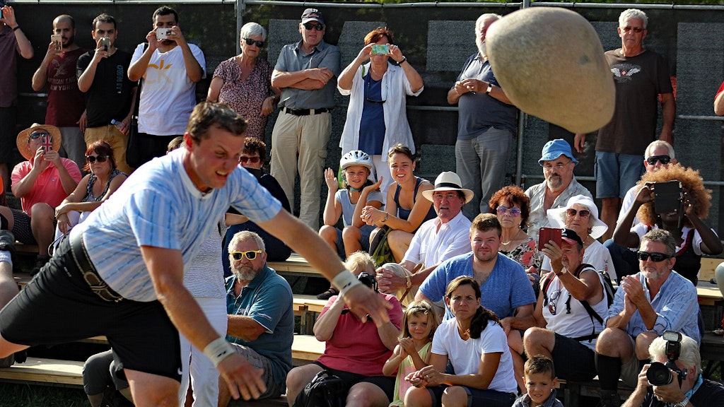 A man throws a large stone while spectators watch and take photos.