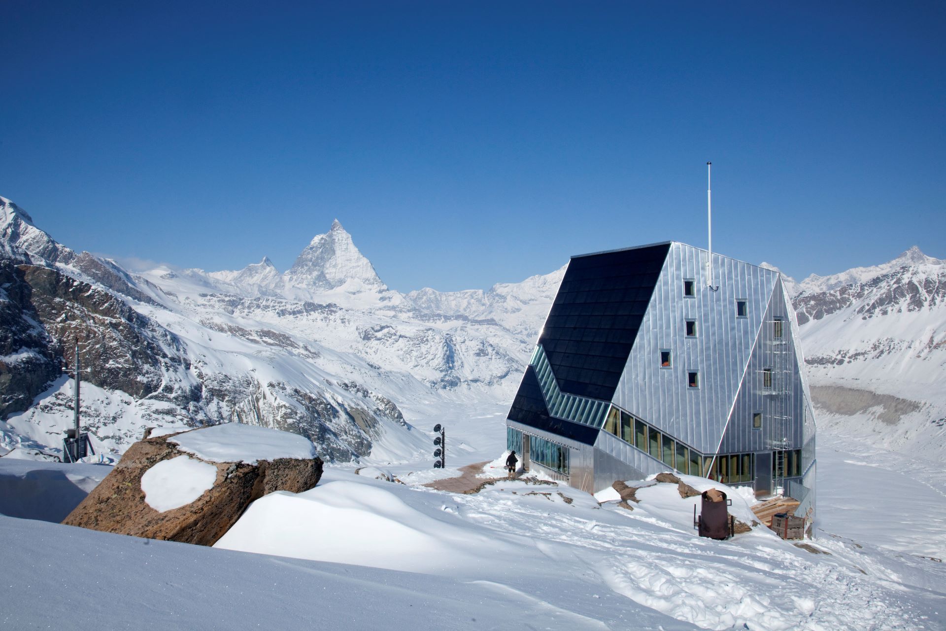 Picture of the Monte Rosa hut in winter with mountains in the background.