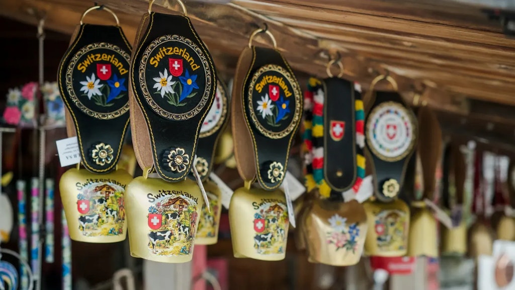 Hanging Swiss decorative bells with floral designs, edelweiss, and the Swiss flag, displayed in a wooden souvenir shop.