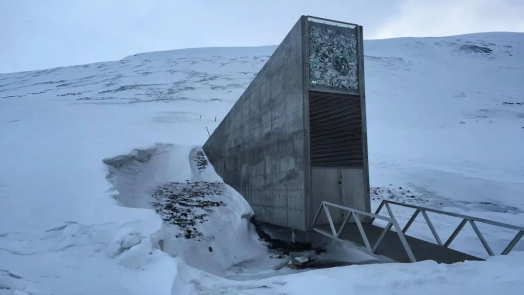 Triangular concrete building partially buried in snow, with decorative panel and metal walkway.