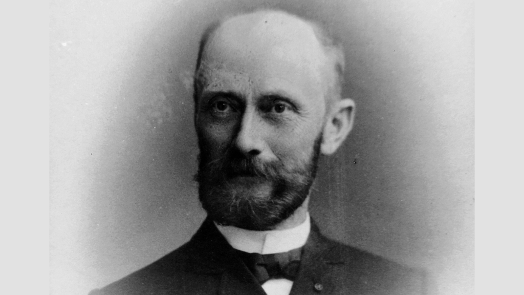 Black and white portrait of a bearded man wearing a dark suit, light shirt and bow tie, photographed from the front.