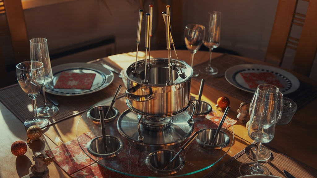 Set table with a stainless steel pot for fondue bourguignonne, wine glasses and plates with red napkins.