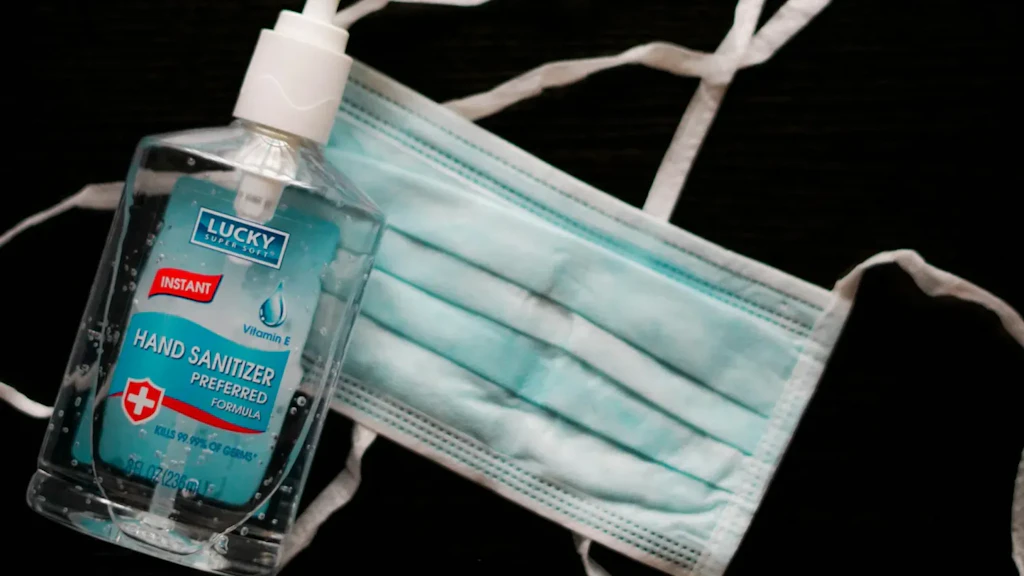 Bottle of Lucky hand sanitiser gel with pump and blue surgical mask with white elastic straps on a black background. 
