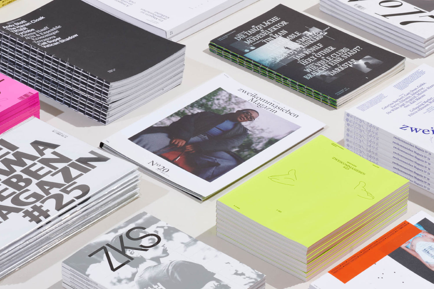 Several stacks of graphically designed magazines are arranged on a white table, viewed from above.