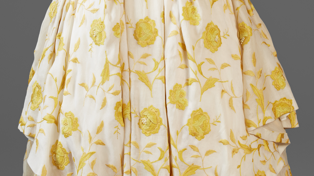 Detail of a light fabric embroidered with yellow floral patterns and stylised leaves.