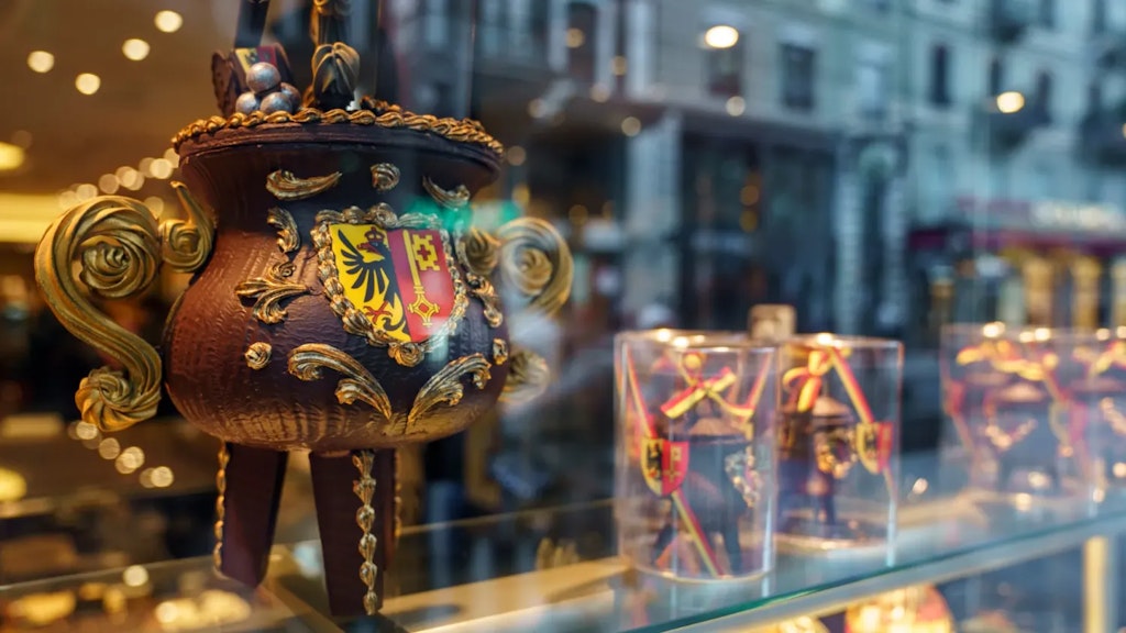 Large chocolate cauldron with the Geneva coat of arms displayed in a shop window, with smaller packaged cauldrons in the background.