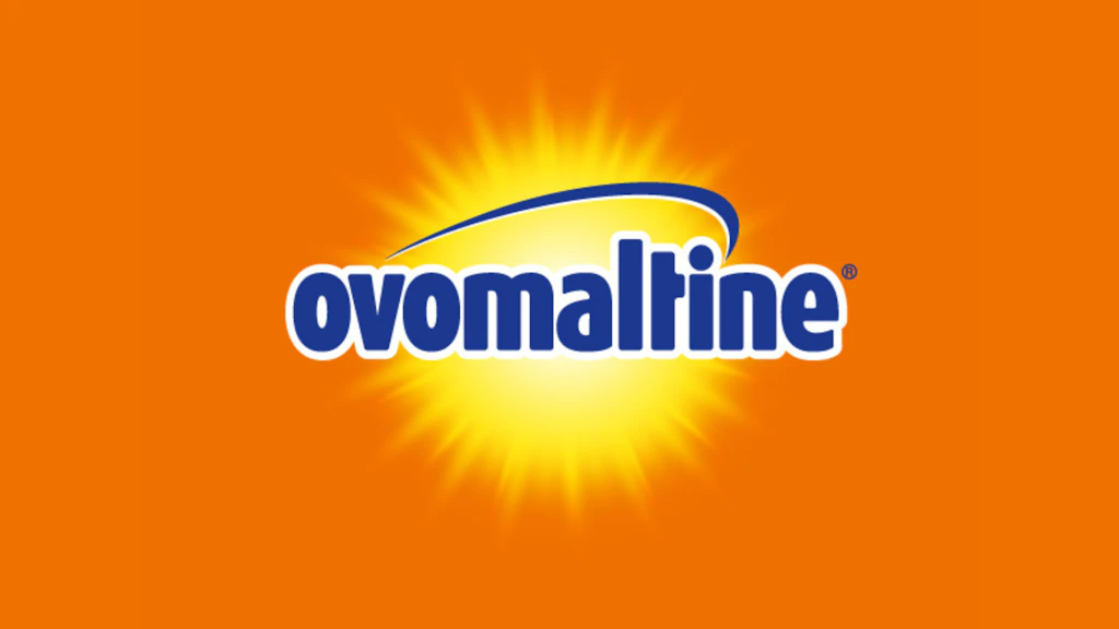 Ovomaltine logo in lowercase blue letters outlined in white over a bright yellow sunburst design on an orange background.