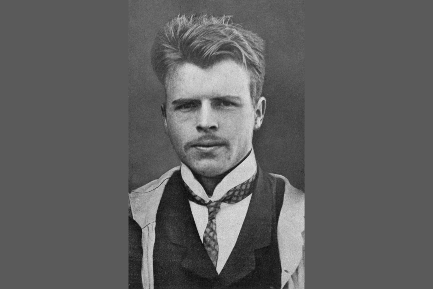 Black-and-white portrait of a young man circa 1910 with brush-cut hair, wearing a shirt and loosely tied tie, face shown in a frontal close-up.
