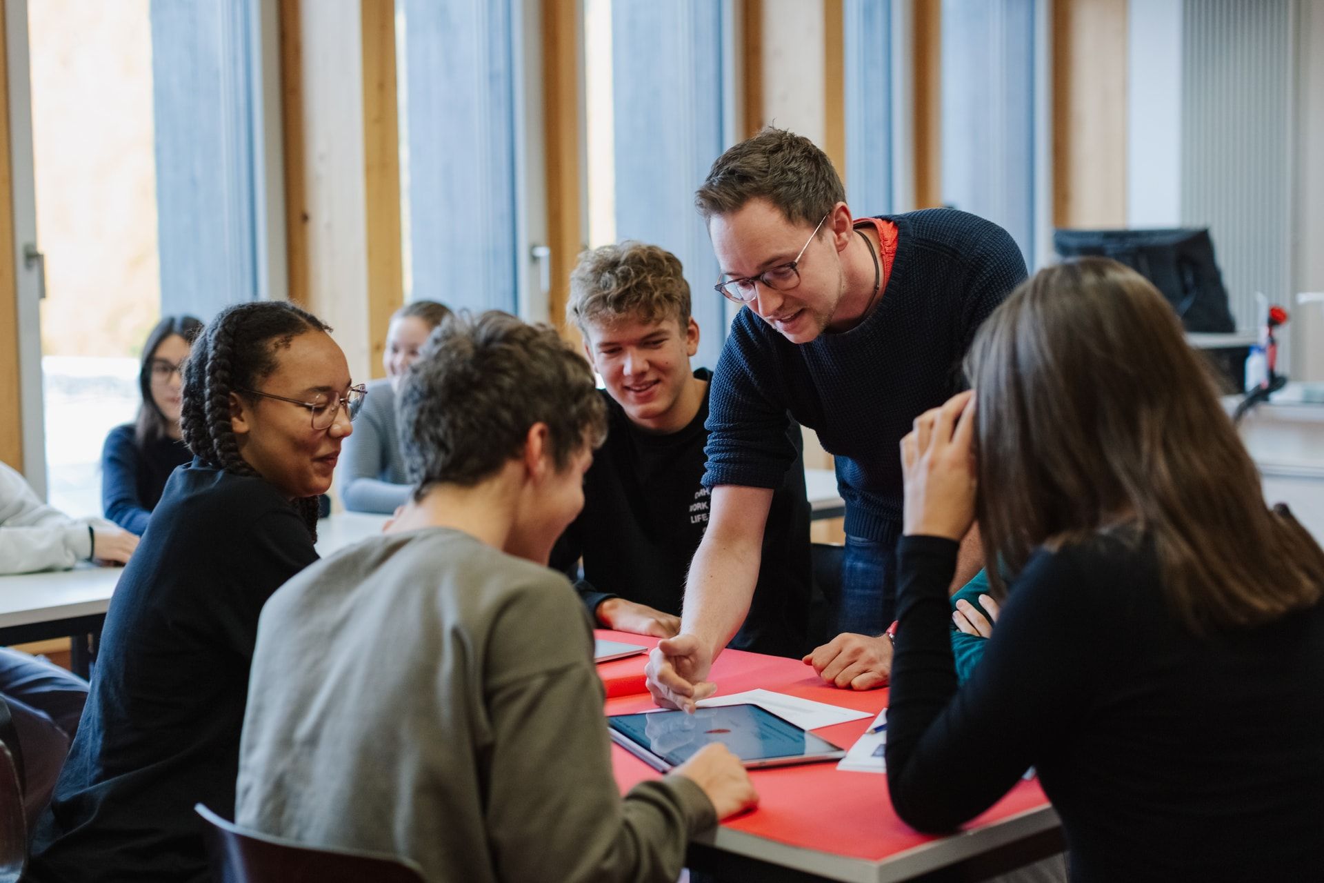 Five students seated together at a table with a tablet that the teacher is using to explain something.