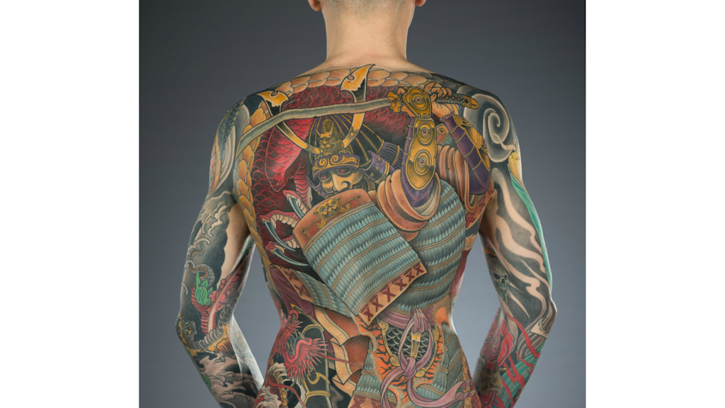 Photograph showing a tattooed back covered with a colourful design of a warrior in armour holding a sword and shield.