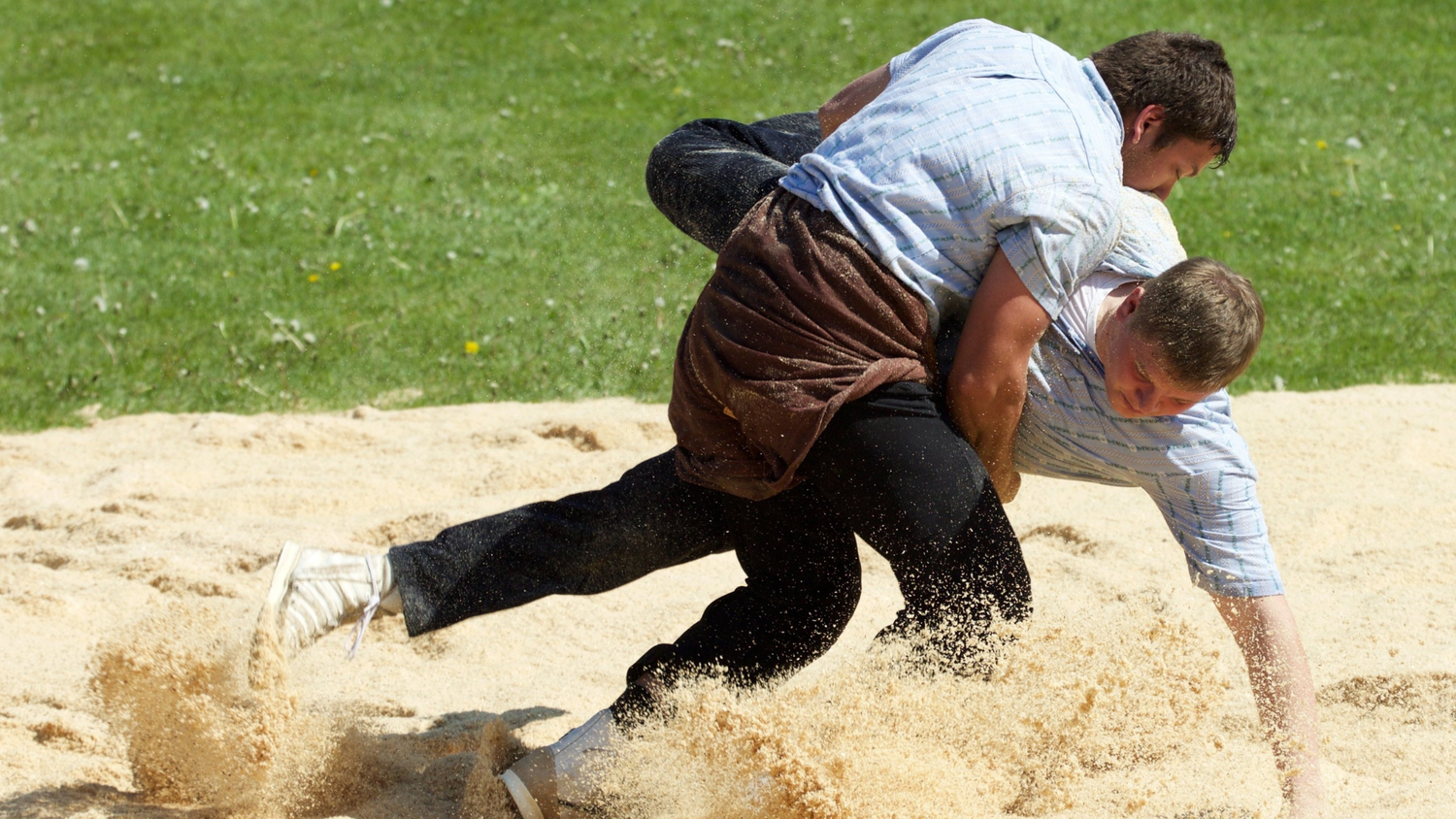 Two Schwingen wrestlers competing in a sawdust ring, a traditional Swiss form of outdoor wrestling.