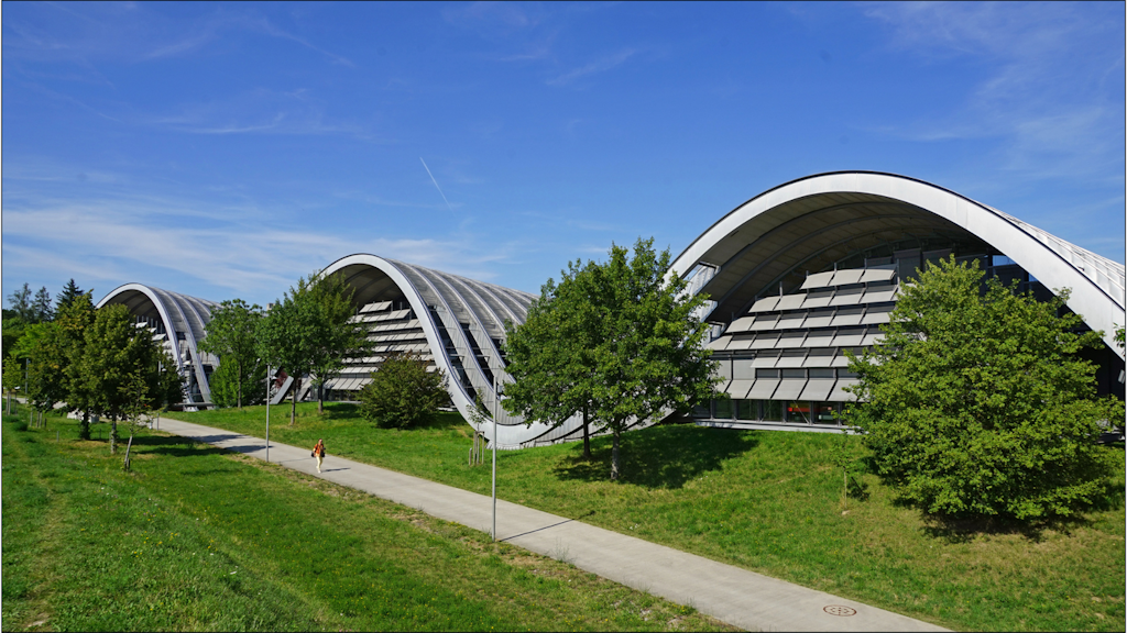 Modern building with wave-shaped roofs housing the Zentrum Paul Klee in Bern, surrounded by trees and green areas under a blue sky.