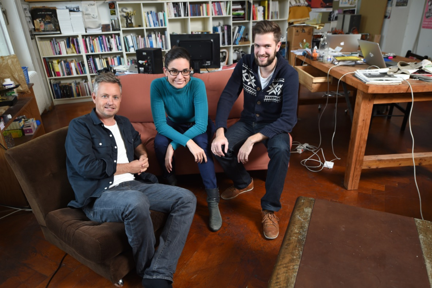 Three people seated in an office with bookshelves in the background, smiling towards the camera.