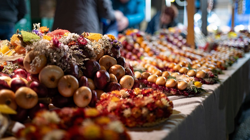 A market stall displays a colorful selection of onion braids decorated with flowers.