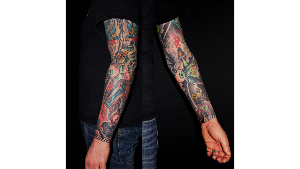 Photograph showing both arms of a person tattooed from hand to shoulder, with colourful motifs including eyes, flames, a vehicle and a crown.