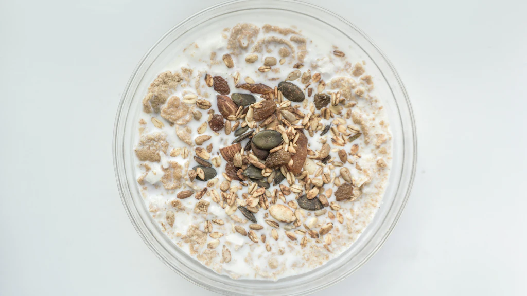 A bowl of Bircher muesli with oats, seeds, nuts, and apple pieces in milk, viewed from above on a light background.