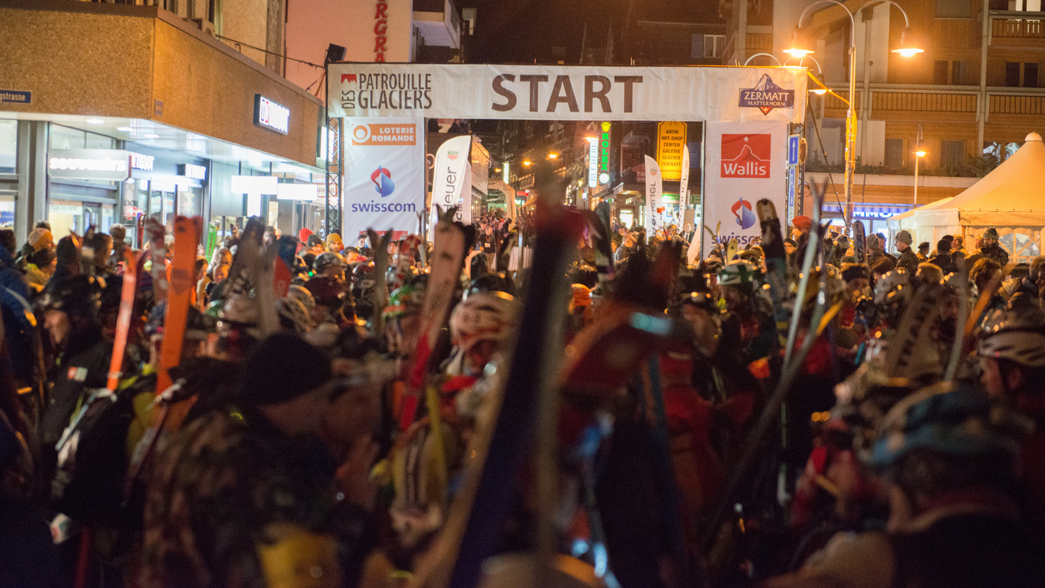 Night start in Zermatt for the Patrouille des Glaciers, with participants in ski gear under an arch marked «Start».