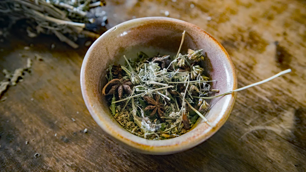 Ceramic bowl containing a mixture of dried herbs and plants, placed on a wooden surface. 