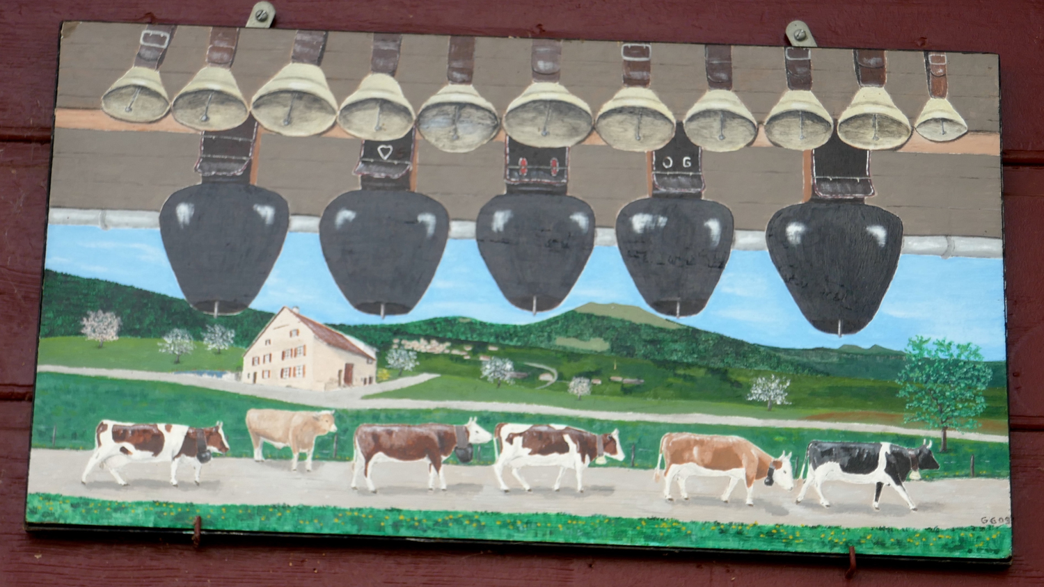 Pintura rústica colgada en una pared de madera, representando cencerros suspendidos y un paisaje alpino con una granja y vacas que pastan.