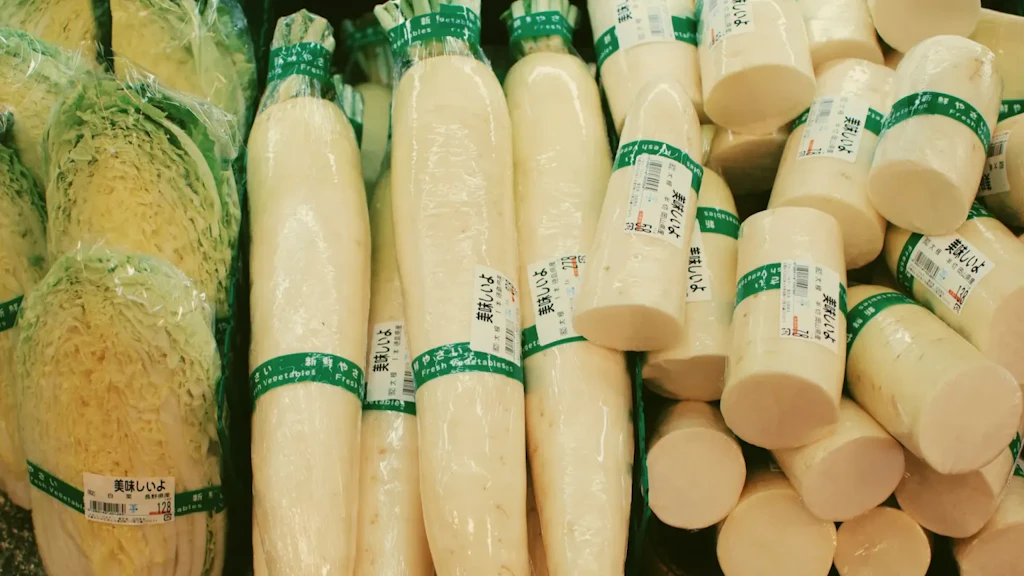 Rábanos daikon blancos y coles envueltos individualmente en film plástico con etiquetas en japonés sobre fondo verde.