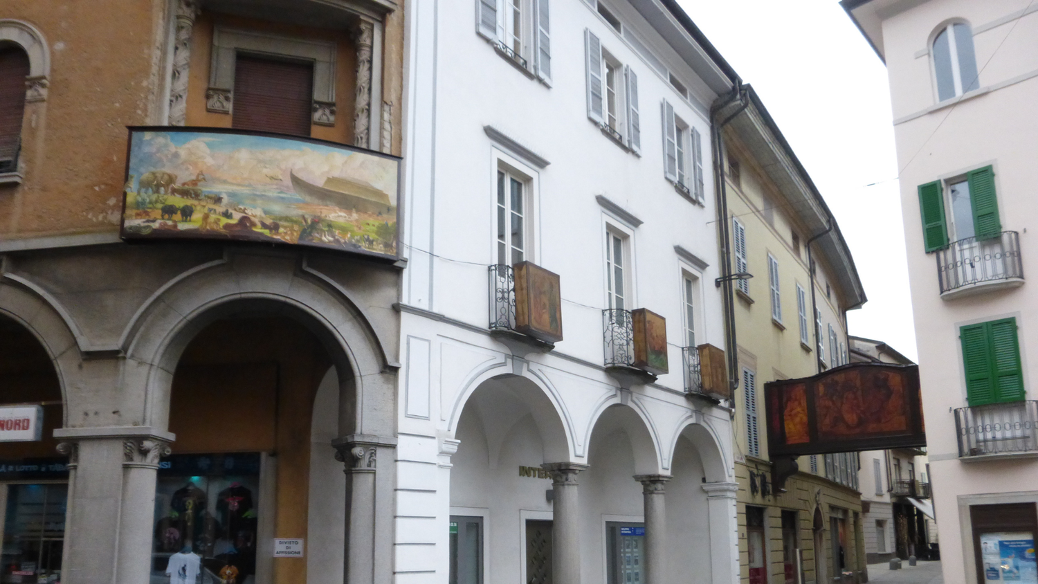 Calle histórica con arcadas y edificios decorados con pinturas religiosas en Mendrisio, Suiza, donde tienen lugar los desfiles tradicionales de Semana Santa.