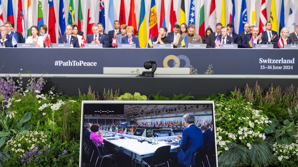 Foto de la conferencia internacional #PathToPeace que tuvo lugar en Suiza en 2024 y que contó con la participación de delegados de alto rango, sentados delante de banderas nacionales y de un monitor con imágenes en directo de la videoconferencia.