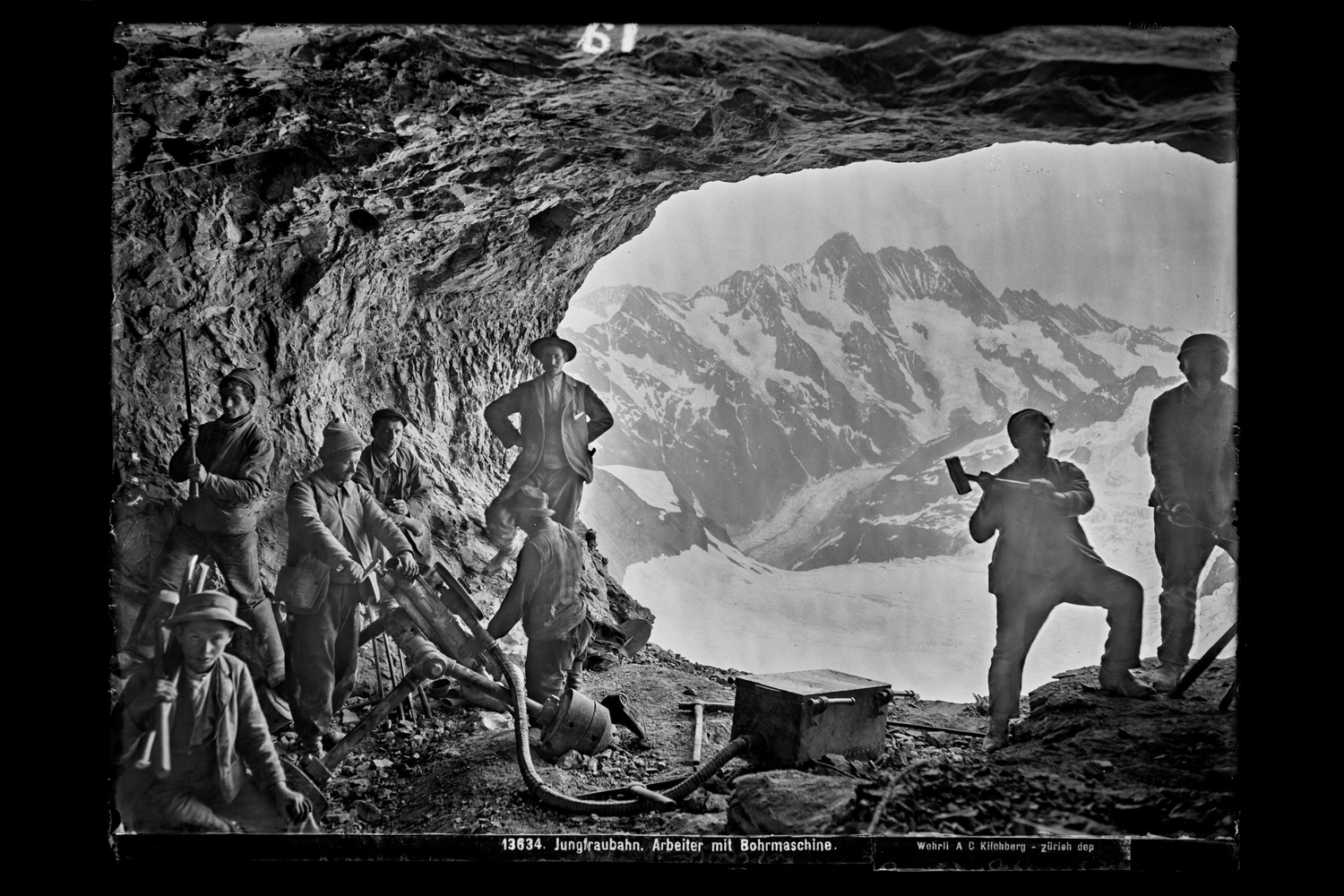 Trabajadores en una cueva con máquinas de perforación, montañas nevadas al fondo.