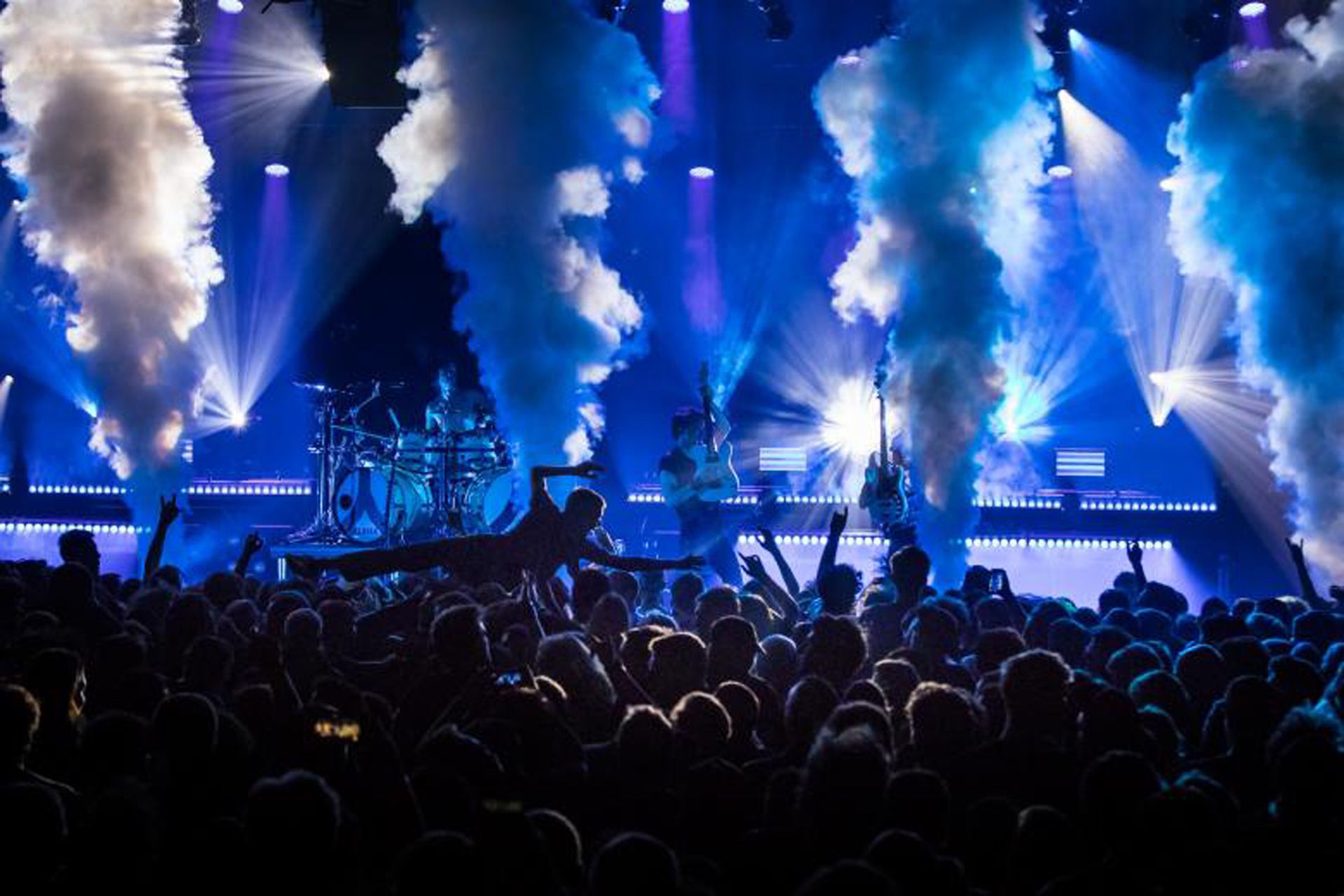 Un concierto con luces brillantes, humo y una multitud en primer plano.