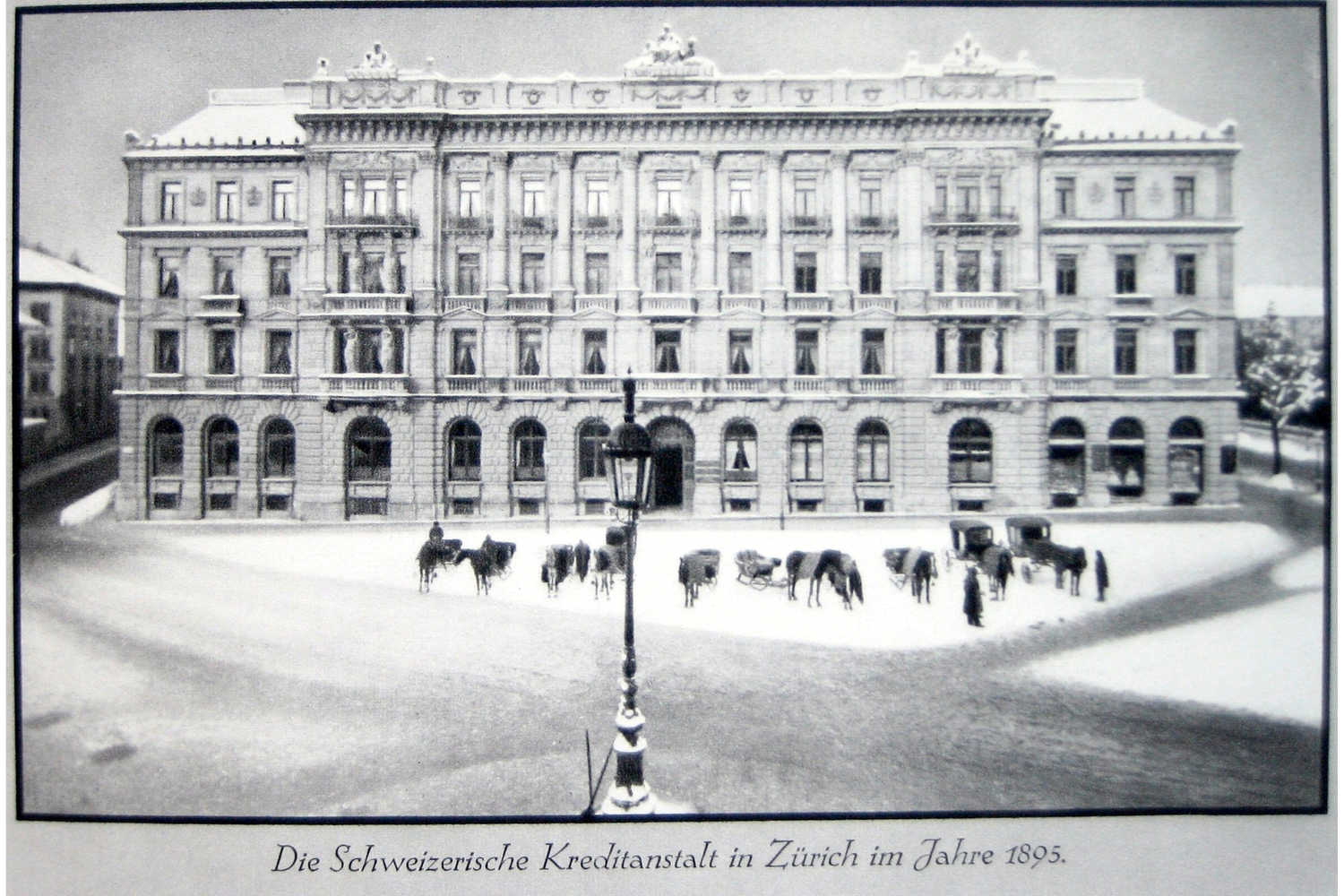 Fachada de la Schweizerische Kreditanstalt en Paradeplatz de Zúrich en 1895, plaza nevada con carruajes y viandantes ante el edificio clásico.