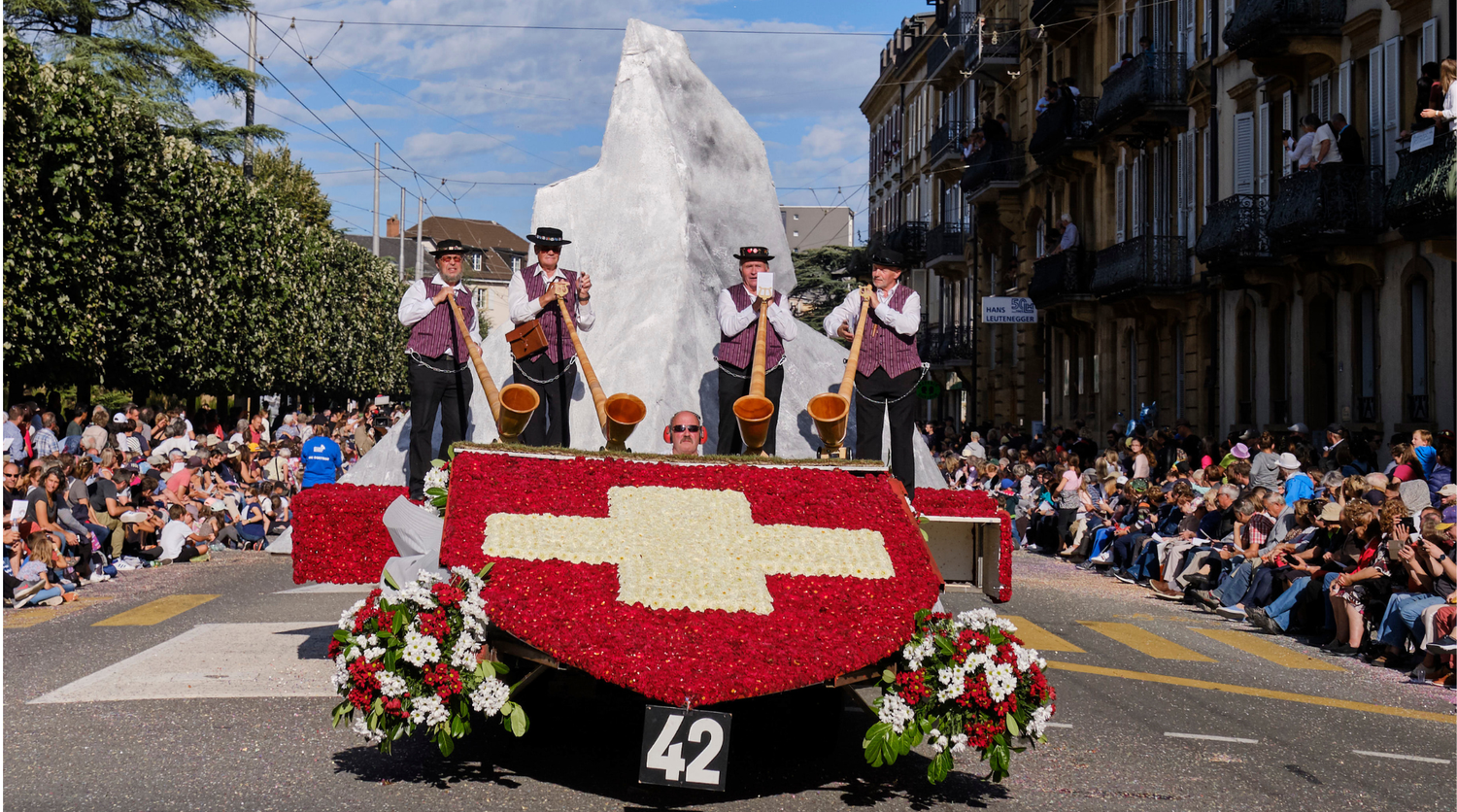 Carroza floral con cruz suiza y tocadores de cuerno alpino desfilando en la Fiesta de la Vendimia de Neuchâtel.