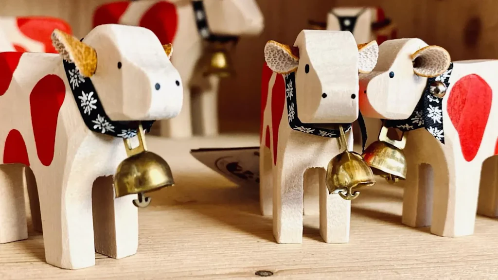 Figurines de vaches en bois avec taches rouges et cloches, disposées sur une surface en bois, vues de face et légèrement de côté.