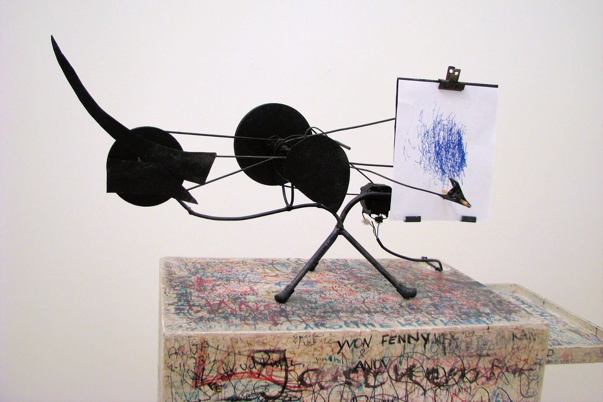 Sculpture Metamatic n°10 de Jean Tinguely (1959): mécanisme en métal noir articulé avec pinceau et feuille de papier griffonnée, posé sur un socle graffité.