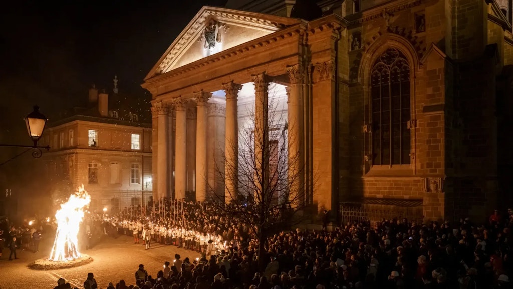Grande foule rassemblée de nuit devant une cathédrale éclairée, avec un grand brasier allumé au premier plan et un cortège en costumes historiques aligné devant le bâtiment.