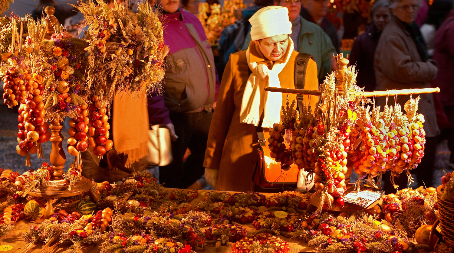 Femme regardant un étal de marché illuminé, rempli de guirlandes d'oignons décorées de fleurs séchées, entourée d'autres visiteurs.