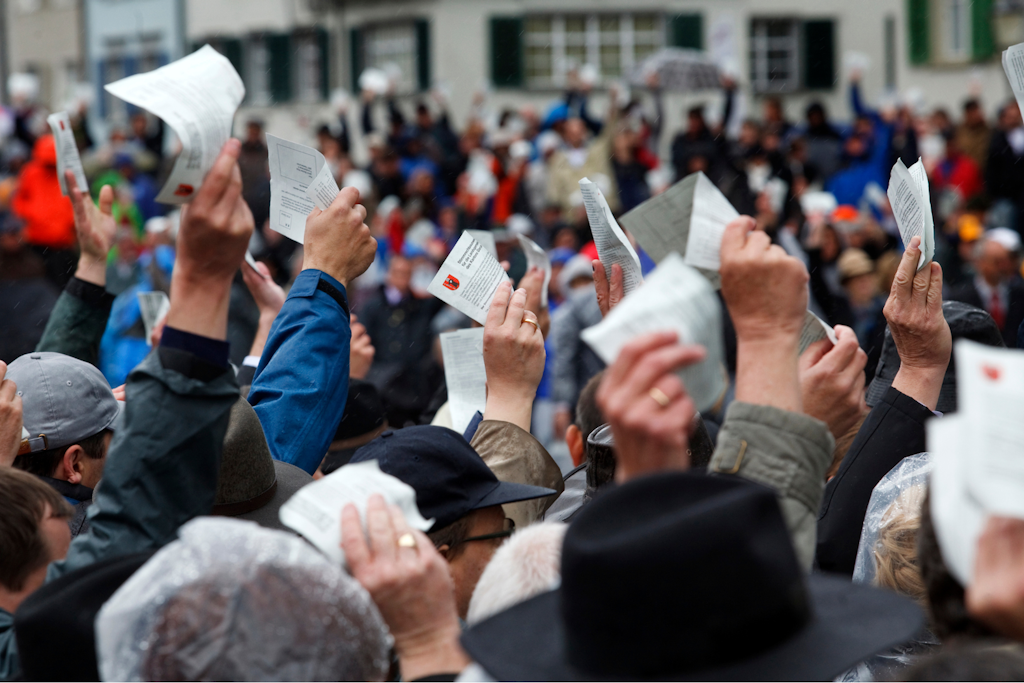 Plan rapproché de nombreuses mains levées dans une foule, tenant des bulletins de vote de papier clair.