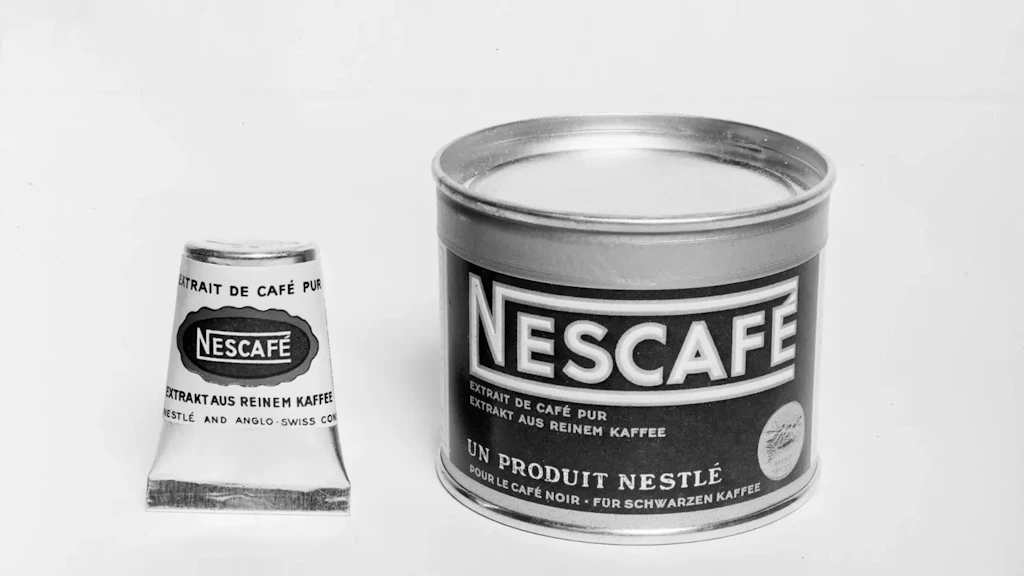 Photographie en noir et blanc de deux contenants Nescafé: un tube conique et une boîte cylindrique métallique. 