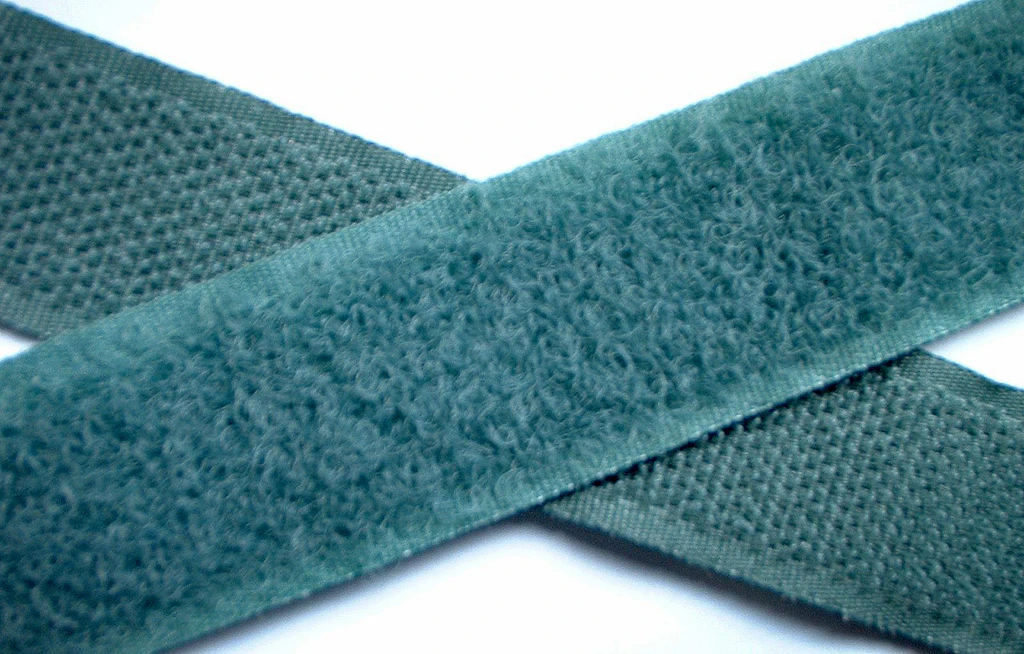 Deux bandes de velcro vert croisées sur fond blanc: l'une avec crochets, l'autre avec boucles fibreuses. 