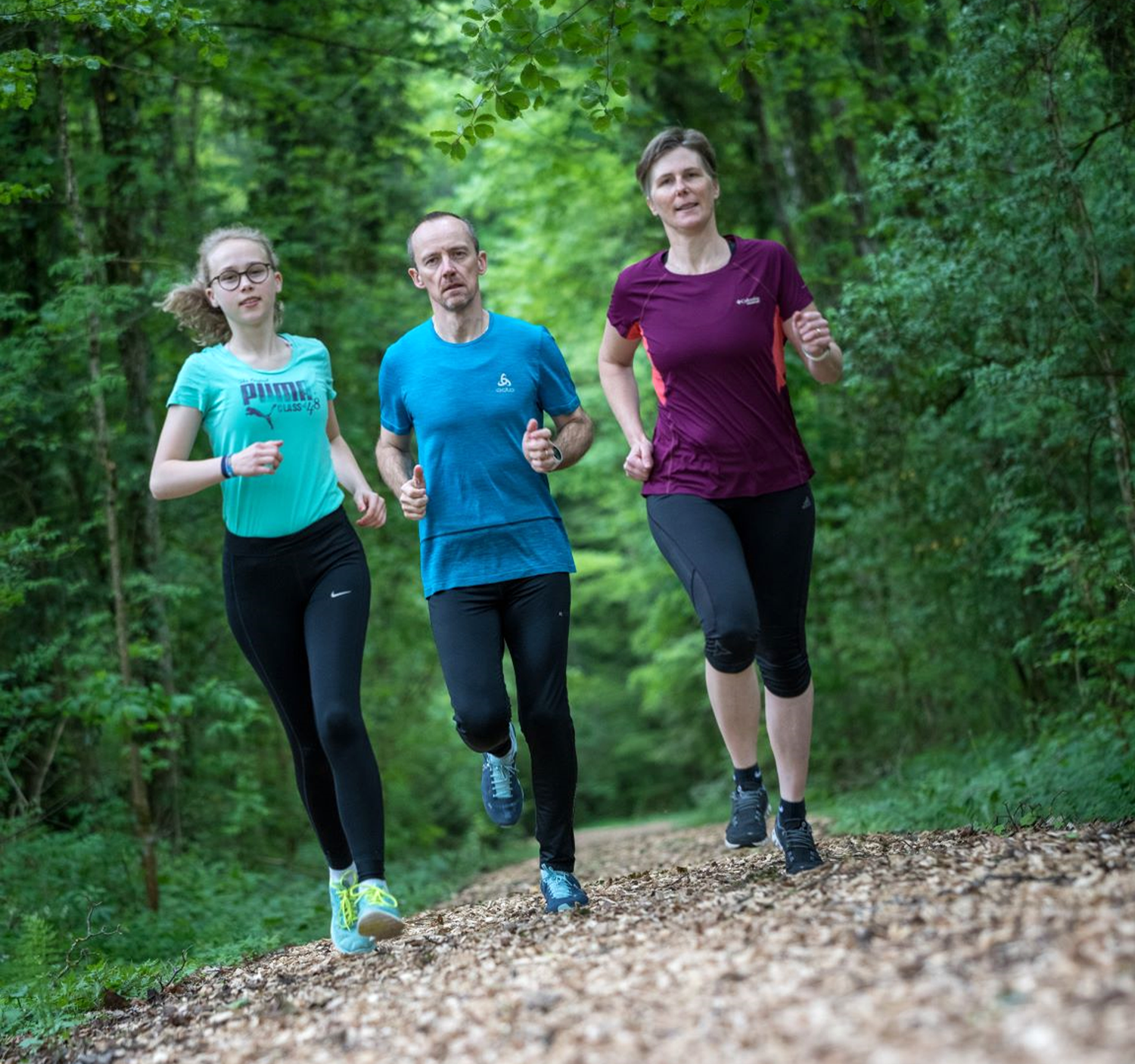 Trois personnes courent côte à côte sur un chemin forestier.