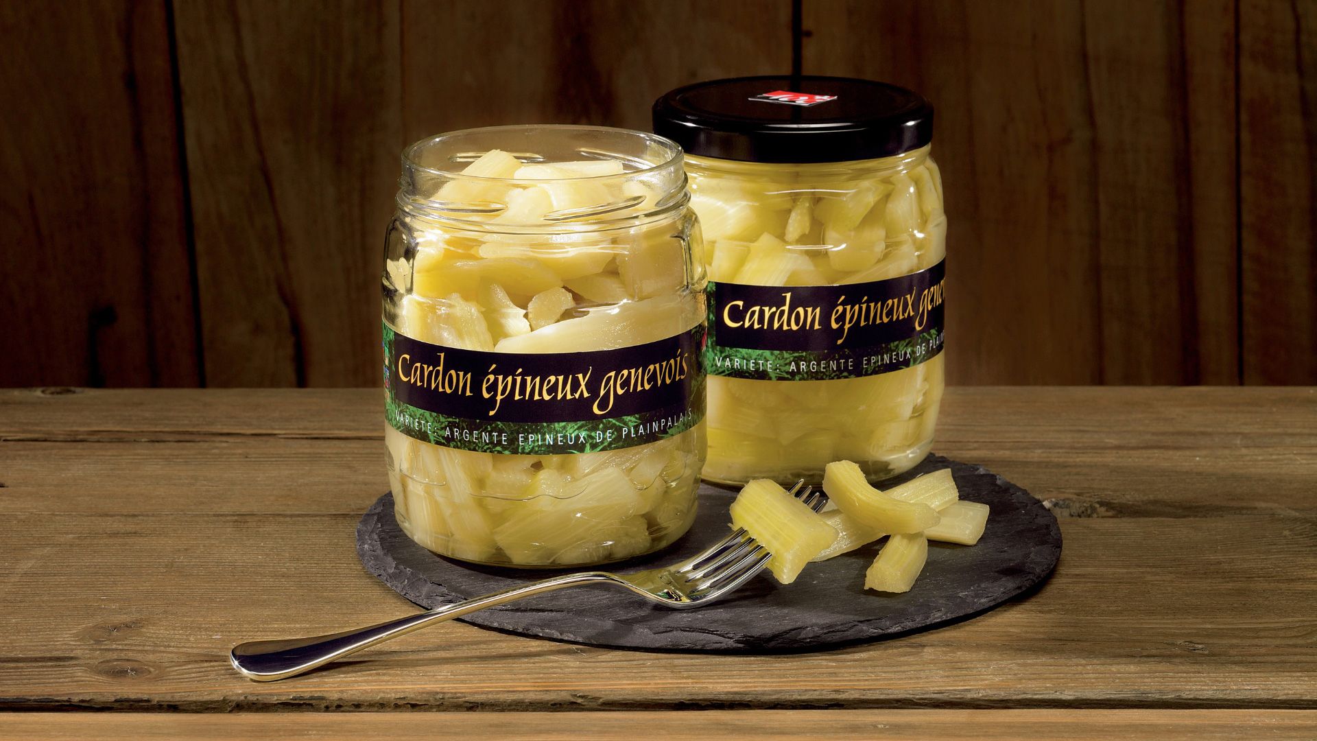 Deux bocaux de cardons épineux genevois sur une table en bois, avec une fourchette et quelques morceaux de cardons à côté.