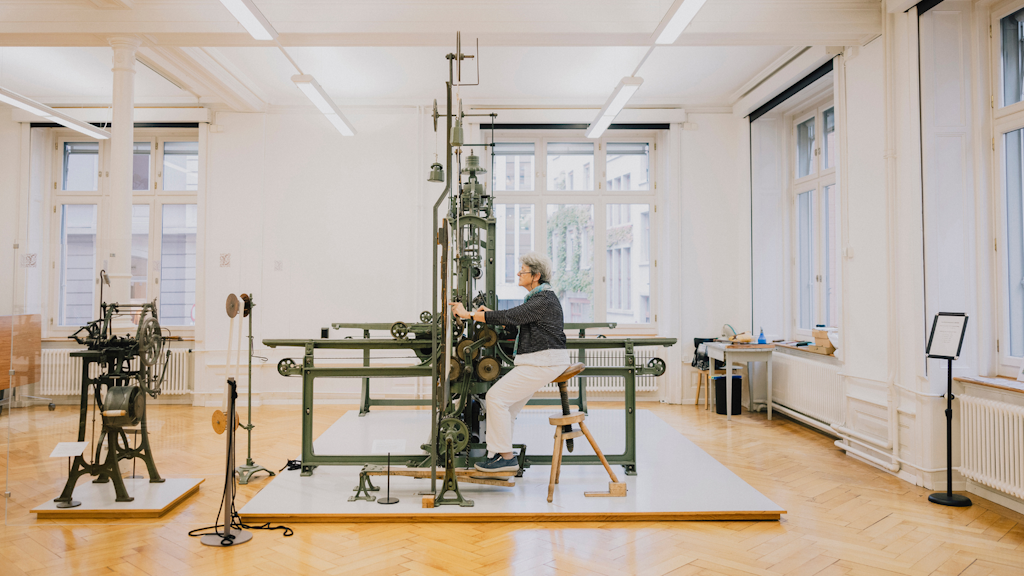 Femme assise devant une machine textile ancienne dans une salle lumineuse du musée du textile de Saint-Gall.