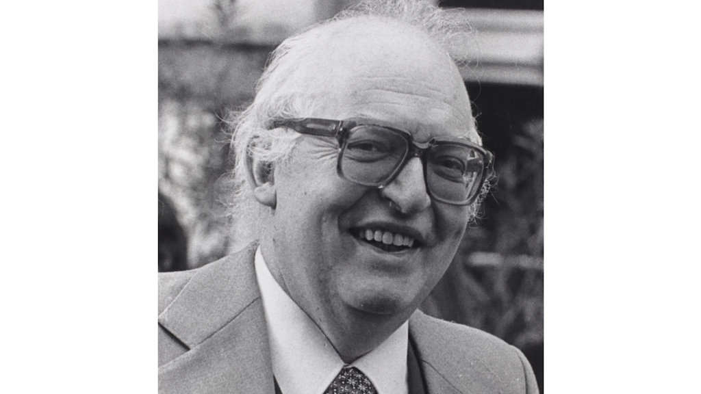 Ritratto in bianco e nero di Friedrich Dürrenmatt. Uomo anziano sorridente in giacca e cravatta, capelli bianchi e occhiali spessi, primo piano in bianco e nero.